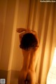 A naked woman standing in front of a lamp.