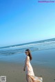 A woman in a long dress walking on the beach.