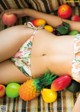 A woman in a bikini laying on a blanket surrounded by fruit.